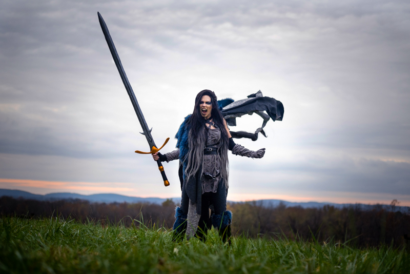 A woman dressed as Yasha from Critical Role screams at the sky with her cape blowing out behind her