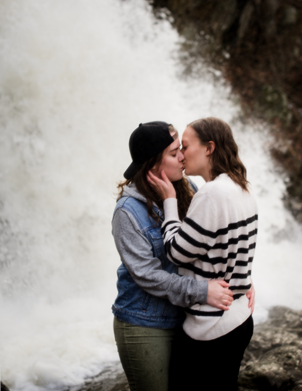 A same-sex couple kisses in front of a waterfall in Harpers Ferry
